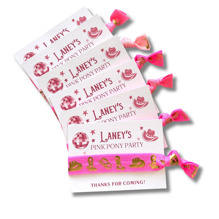 A set of pink hair ties with the text "Laney's Pink Pony Party" printed on them, along with a pink ribbon and a small image of a pink pony.